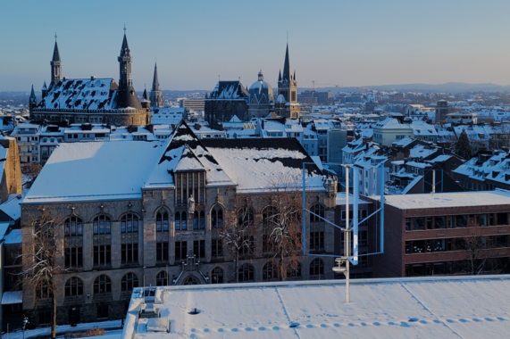 Photo of Aachen with the old town in the background. A model of the vertical wind turbine is photomounted on a roof in the foreground.