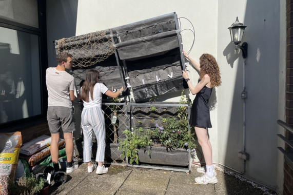 Three people put the upper part of the rectangular metal construction onto the lower part.