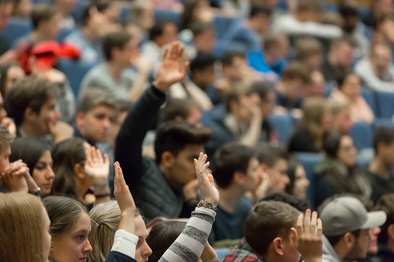 A photo of a crowded lecture hall, several people come forward. The photo is blurred in the background.