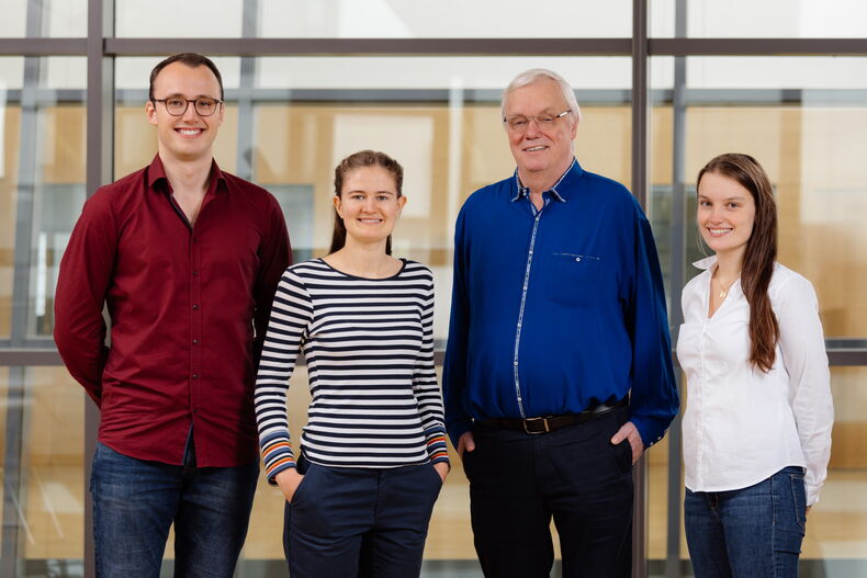 former AStA Officer for Teaching and University Communication Paul Heuermann, AStA Officer for Sustainability and Student Engagement Theresa Janning, Vice-Rector for Teaching Professor Aloys Krieg and former AStA Chairwoman Lena Schrader stand in front of a glass wall. Paul Heuermann red shirt, jeans, Theresa Janning black and white striped sweatshirt and chino pants, Professor Krieg royal blue shirt, jeans, Lena Schrader white blouse, jeans.  They smile into the camera.