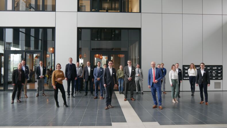 The picture shows participants of the kick-off workshop for the consortium benchmarking "Circular Economy - Lifecycle Management in Manufacturing Companies". Twenty people stand at a distance from each other in an entrance hall.