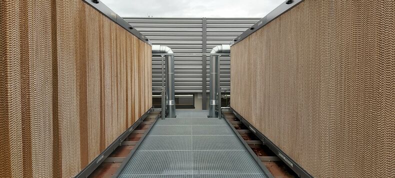 The photo shows a construction on the right and left side of a grating run. At the end, two pipes lead into the recooling unit, one on the right and one on the left. The cooling unit itself is visible from the outside with a fluted structure in light brown.