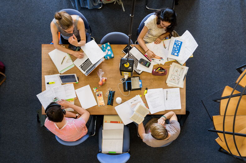 Zwei weibliche und zwei männliche Personen sitzen an einem Tisch. Sicht von oben. Auf dem Tisch sind Lernmaterialien ausgebreitet.