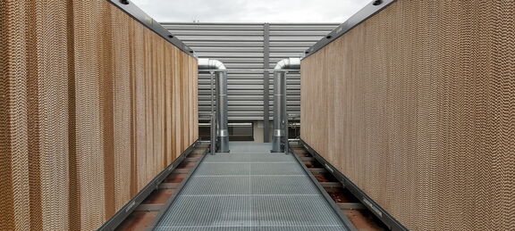 The photo shows a construction on the right and left side of a grating run. At the end, two pipes lead into the recooling unit, one on the right and one on the left. The cooling unit itself is visible from the outside with a fluted structure in light brown.