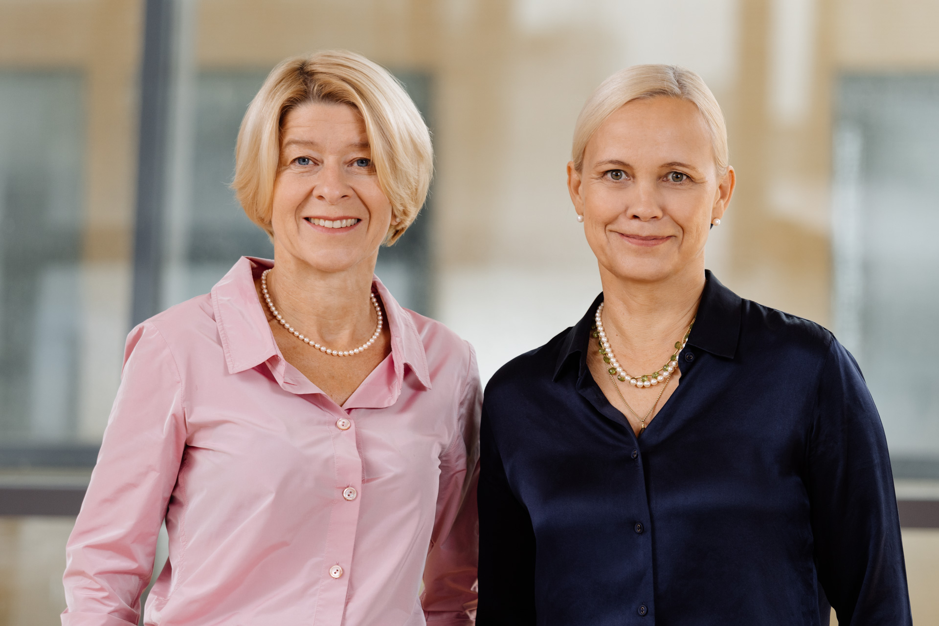 Professor Ute Habel, Prorector for International Affairs and Professor Sabine Brück-Dürkop, Prorec-tor for Human Resources and Young Scientists in front of a glass wall. Professor Habel in pink blouse and black trousers, Professor Brück-Dürkop in dark blue shimmering blouse and black trousers. They smile into the camera.