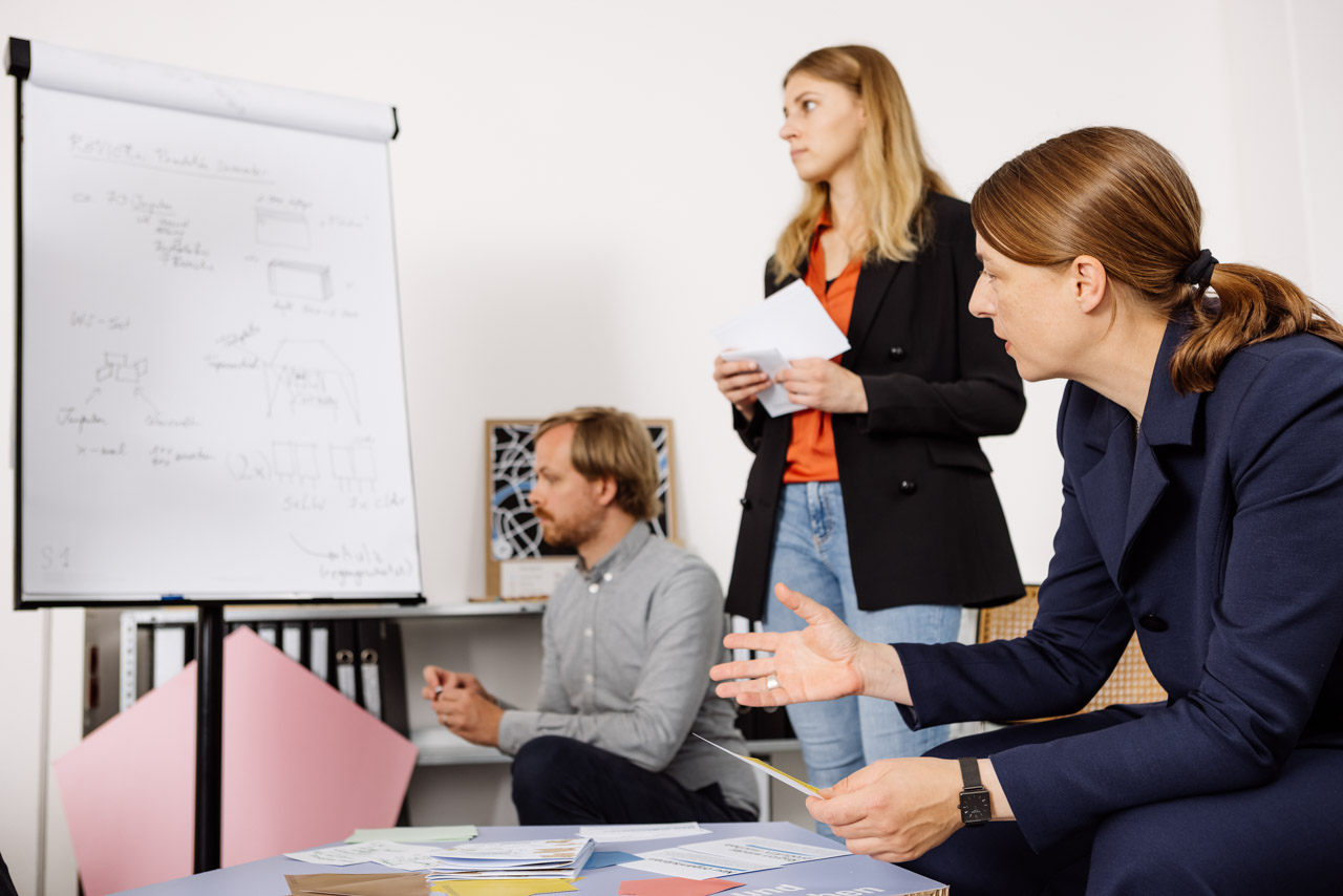 Two females and one male are looking at a flip chart and talking.